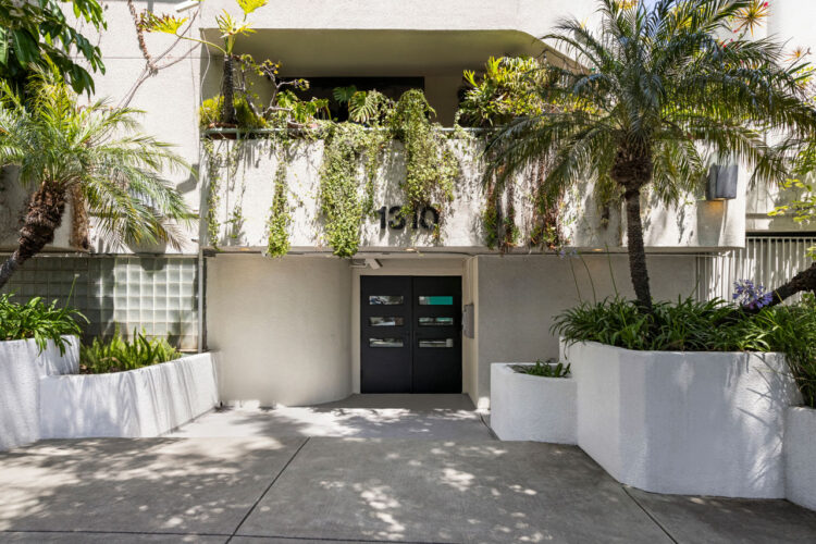 exterior of a grey condo building entrance with palms