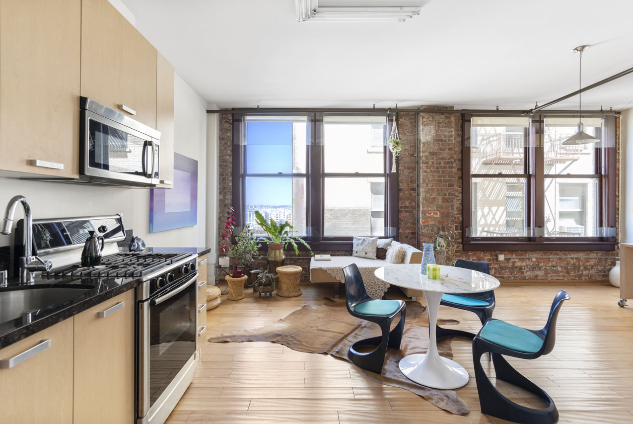 interior of a downtown loft showing wood floors, built in kitchen, dining table, brick wall and windows with a city view