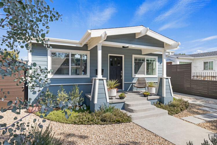 California bungalow with blue siding, front yard with plants, gravel and a walkway