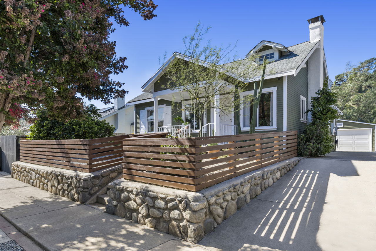 exterior of an olive green california bungalow with a wood fence