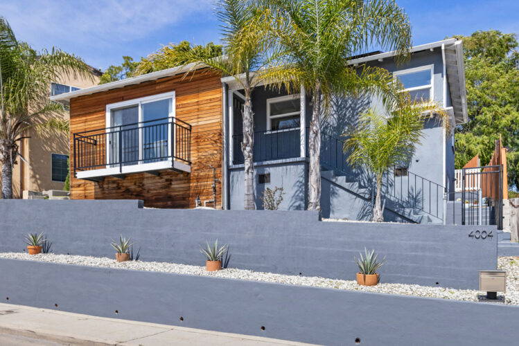 exterior of a traditional home painted blue with wood accents with a blue retaining wall and palm trees