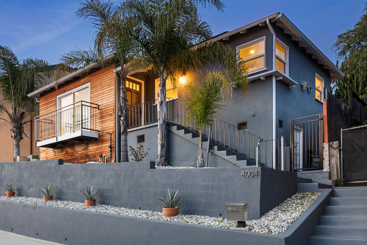 twilight exterior of a traditional home painted blue with wood accents with a blue retaining wall and palm trees