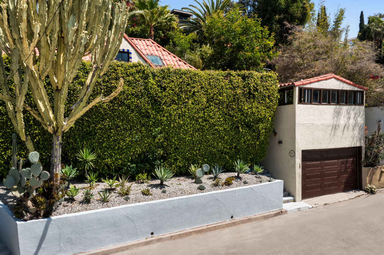 exterior of a spanish style home with a blue retaining wall, cactus, and a green hedge