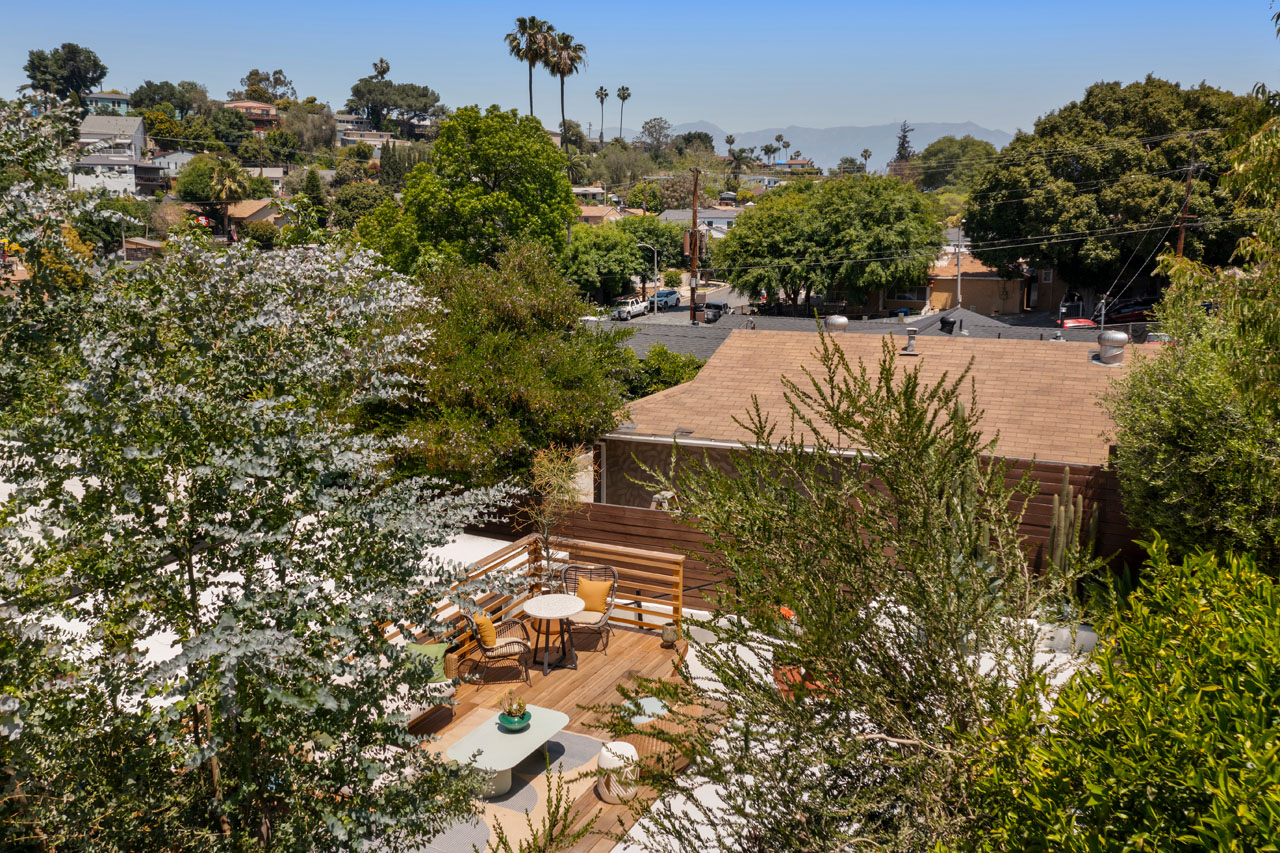 backyard view of a traditional house in el sereno with trees a wood deck and distant views with palm trees