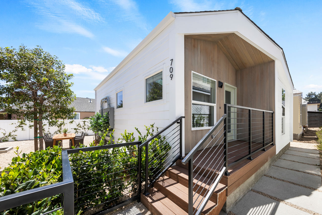 exterior of a one story contemporary tenants-in-common home with white siding and wood detailing and green landscaping in highland park california
