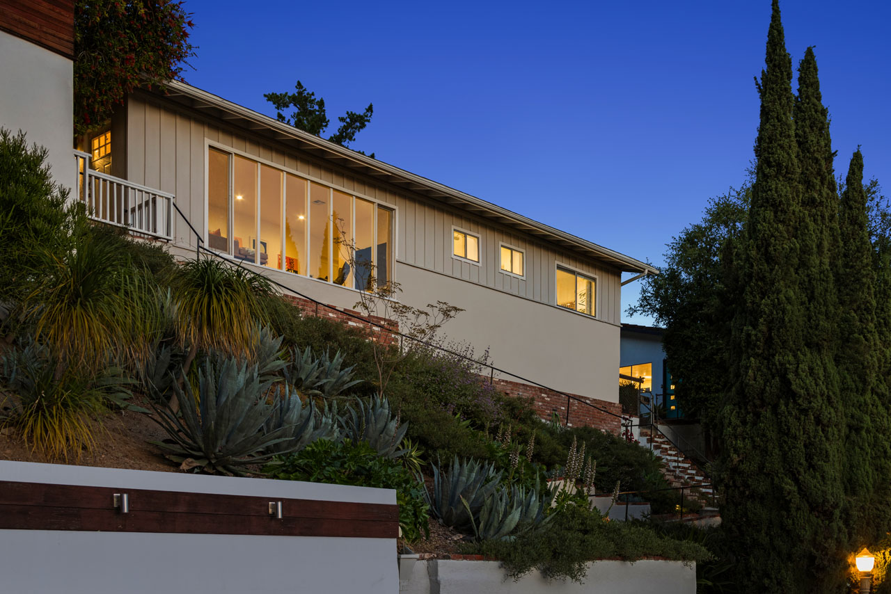 twilight exterior of a mid century style home on a hill with brick accents