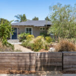 exterior of a traditional home painted green beige with native landscaping and a wood fence