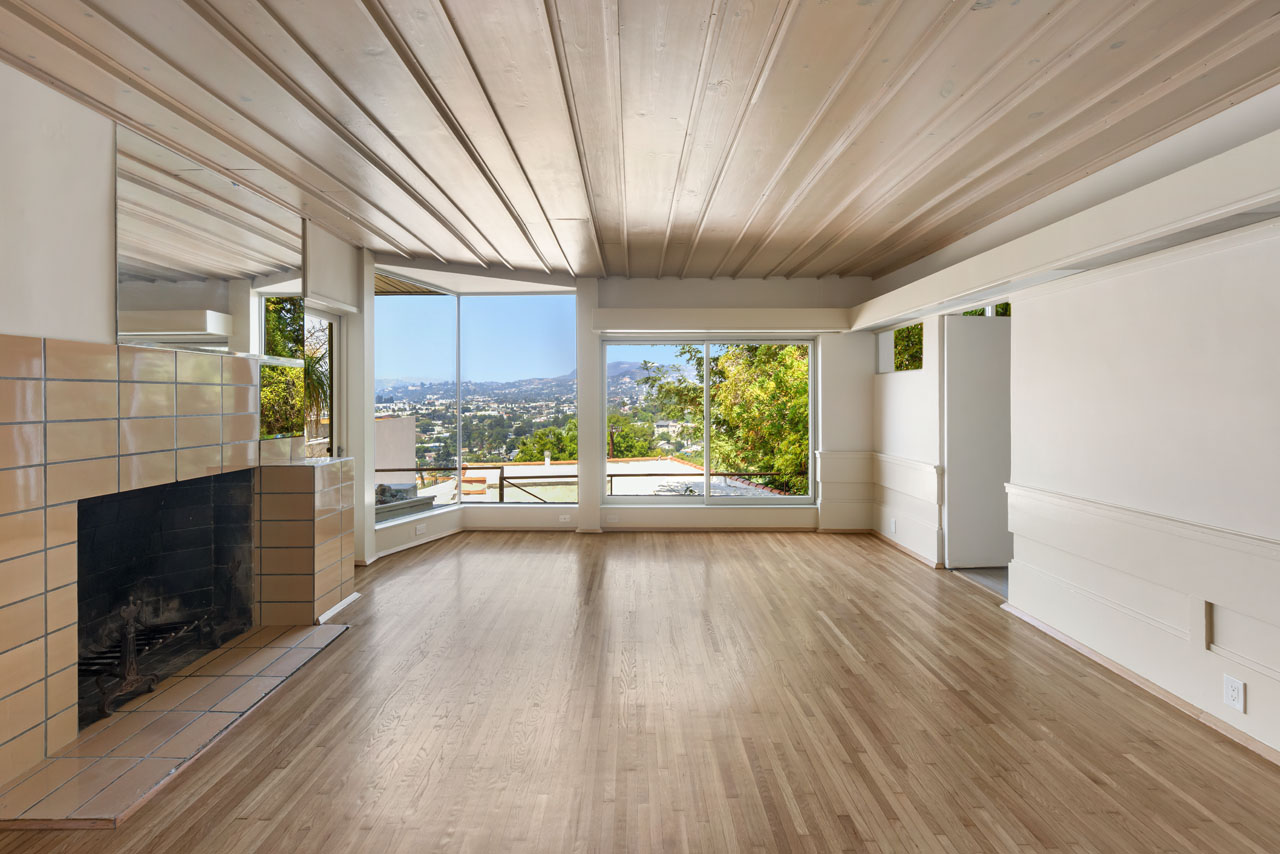 interior of a modernist apartment by rudolf schindler, with a fireplace, wood detailed ceiling and windows with views of the hollywood sign