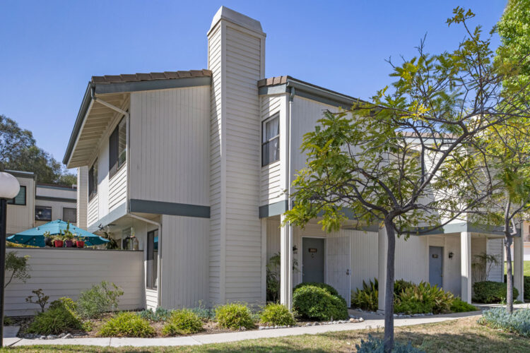 exterior of a two story condo with white beige siding and dark blue trim, trees, bushes and grass