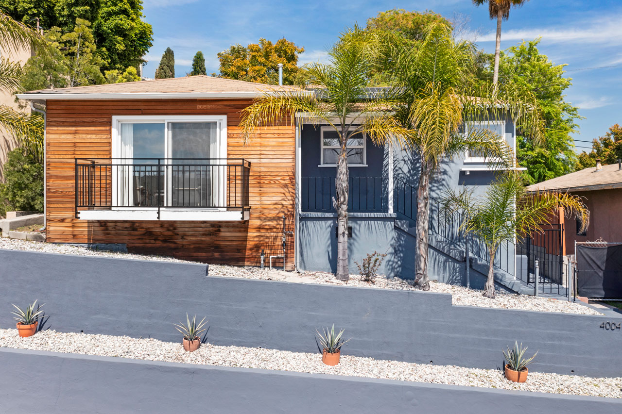 exterior of a traditional home painted blue with wood accents with a blue retaining wall and palm trees