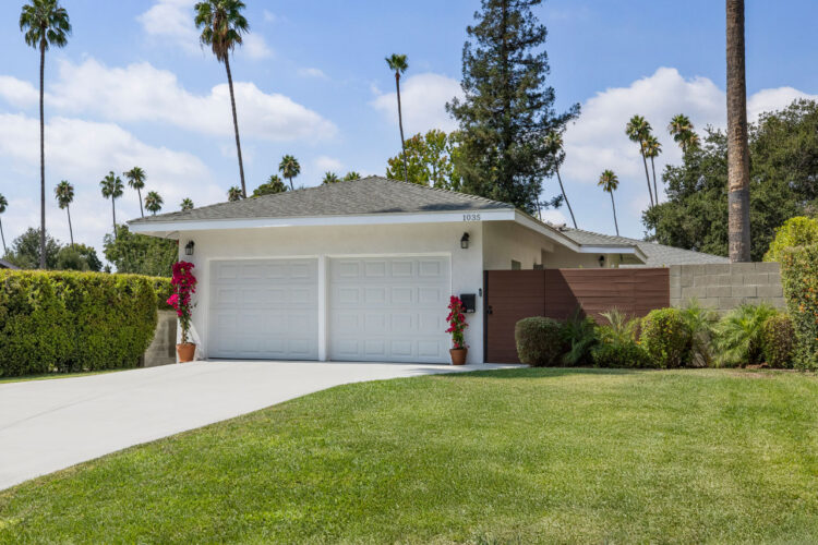 exterior of a four bedroom home with a two car garage green yard and palm trees in the distance