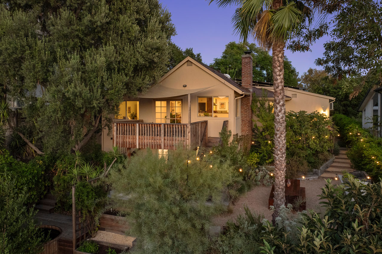 twilight exterior of a traditional home painted beige with a beige wooden fence and verdant landscaping