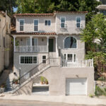 exterior of a three story spanish style home painted grey with white accents and a red tile roof