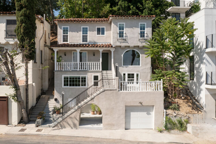 exterior of a three story spanish style home painted grey with white accents and a red tile roof