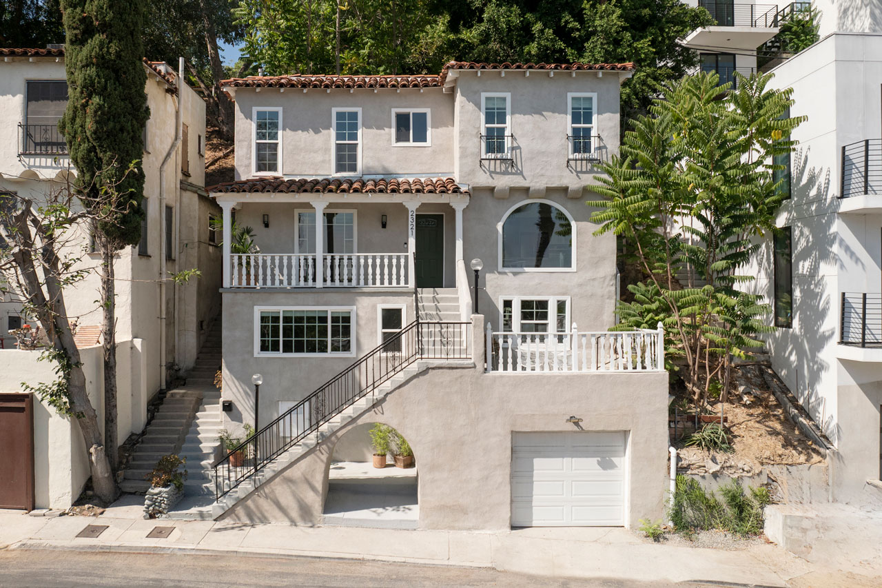 exterior of a three story spanish style home painted grey with white accents and a red tile roof