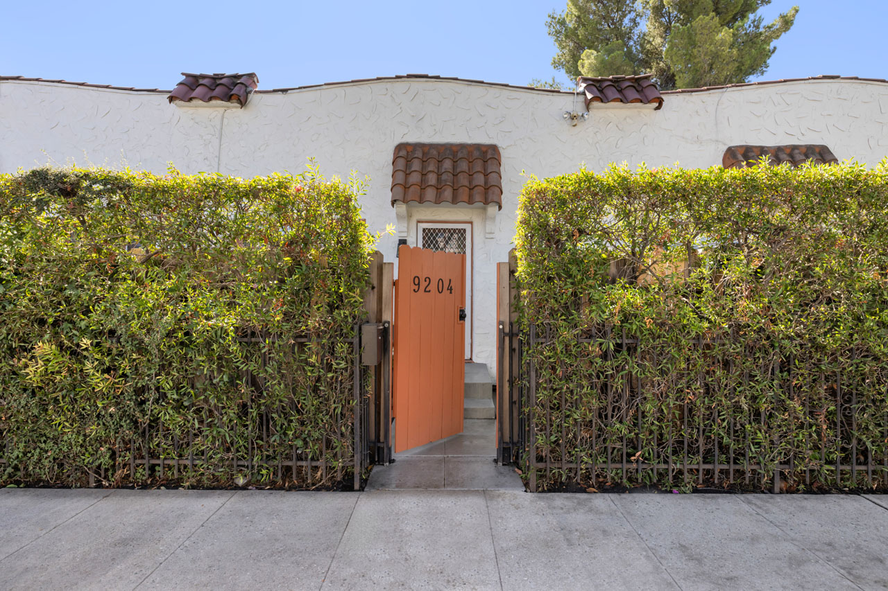 exterior of a spanish style casita condo with green hedge and orange gate