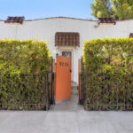 exterior of a spanish style casita condo with green hedge and orange gate