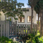 exterior of a white spanish style home with greenery and a brown fence