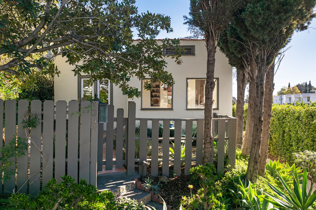 exterior of a white spanish style home with greenery and a brown fence