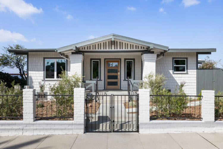 exterior of a craftsman style home painted white with dark green trim a fenced front yard with native plants