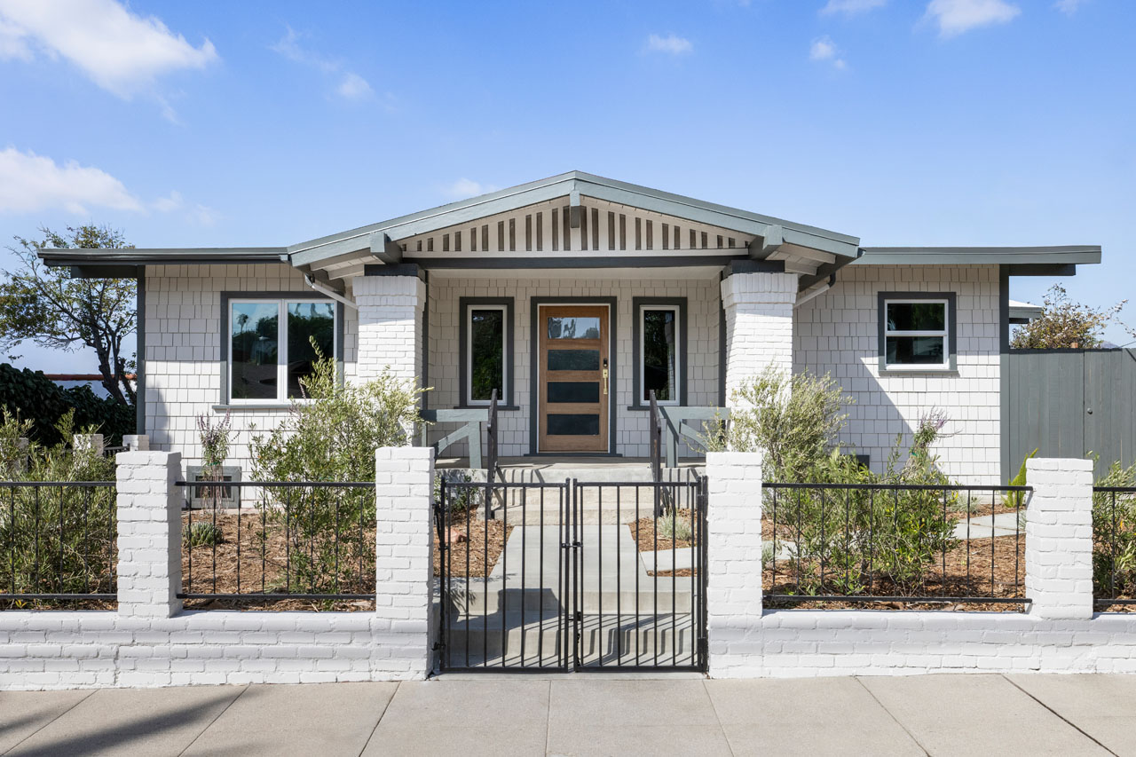 exterior of a craftsman style home painted white with dark green trim a fenced front yard with native plants
