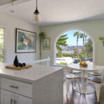 kitchen interior showing a white countertop, circular dining table wiht chairs and arched window with mountain views and palm trees