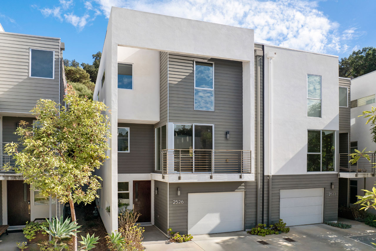 exterior of a small lot single family home, three stories, white and grey with a wood front door and greenery