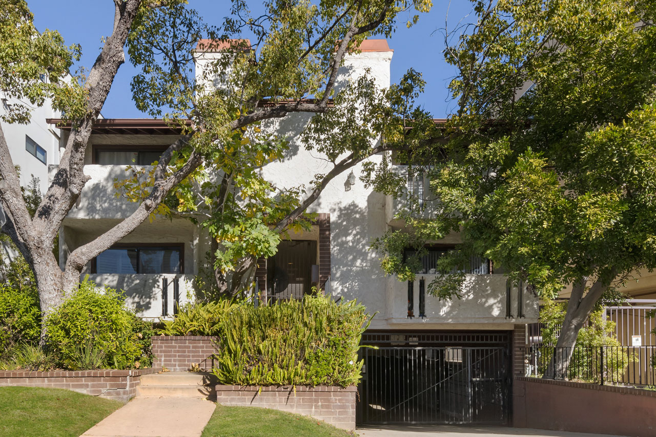 exterior of a condo building painted white with spanish tile roof and green front yard