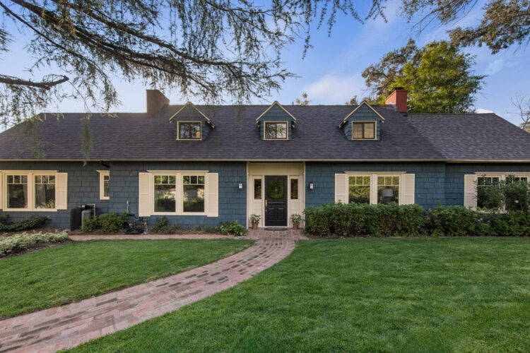 exterior of a large two-story cape cod style home painted blue with white trim a grassy yard and large tree