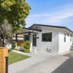 exterior of a traditional one story home painted white with black details a green grassy yard with tree and wooden fence