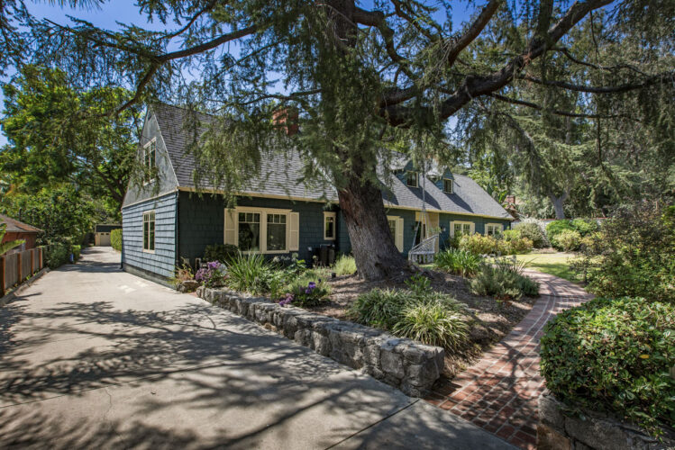 exterior of a large two-story cape cod style home painted blue with white trim a grassy yard and large tree