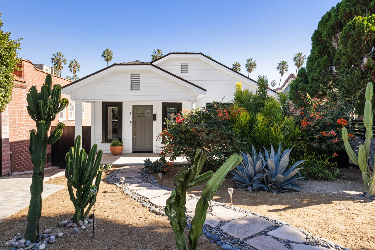 exterior of a renovated traditional home painted white with black trim and a front yard with cactus and native plants