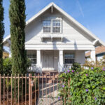 exterior of a two story home paintd white with a red metal fence and three cypress trees
