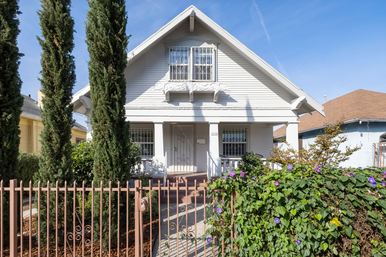 exterior of a two story home paintd white with a red metal fence and three cypress trees