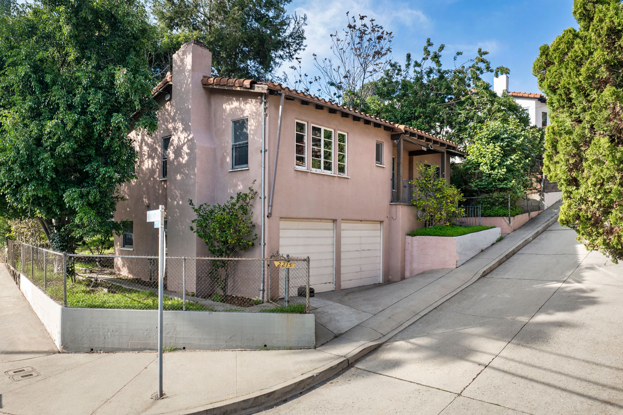 exterior of a two story home, painted pink with spanish tile roof and white garage doors
