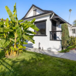 exterior of a traditional style home painted white with black trim, a grass yard with banana tree in the foreground