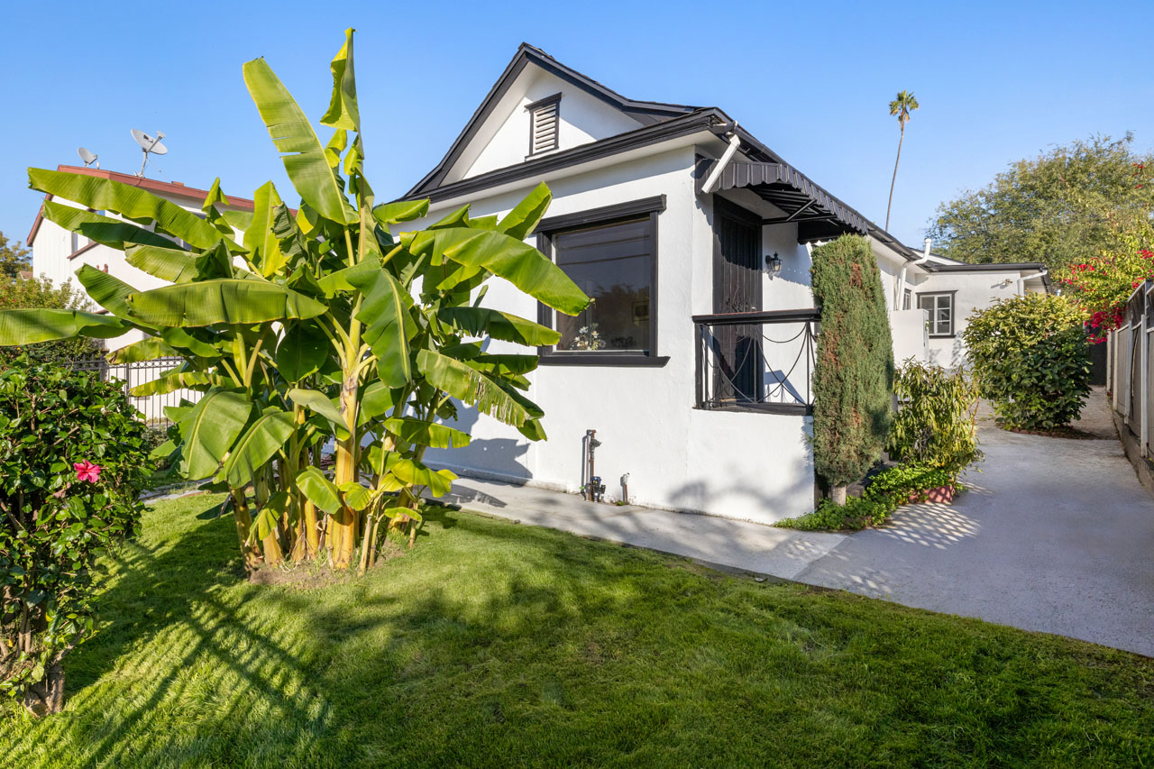 exterior of a traditional style home painted white with black trim, a grass yard with banana tree in the foreground