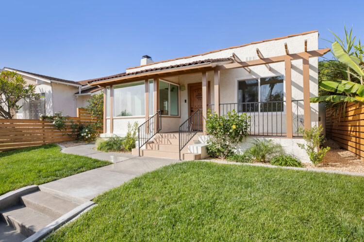 exterior of a one story spanish style home, beige with burnt pink accents and a grass yard