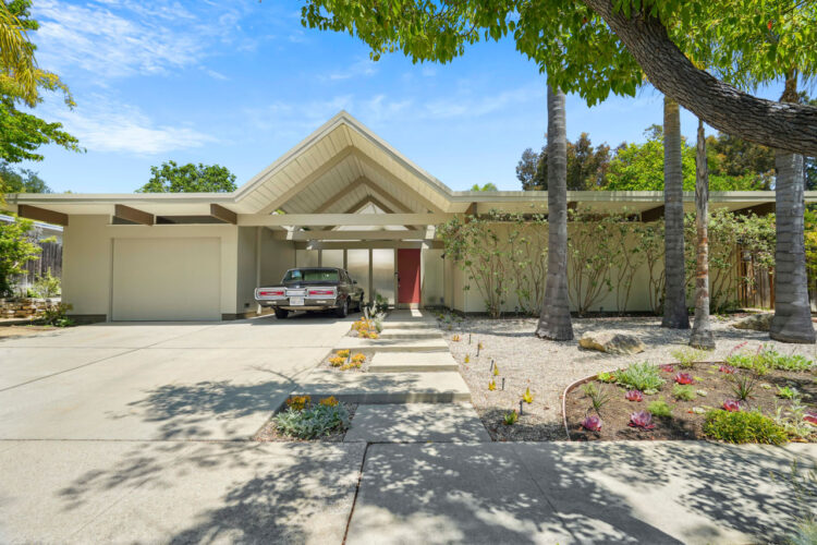 exterior of a mid-century modern home painted slate grey with beige trim and a pitched triangular carport roof