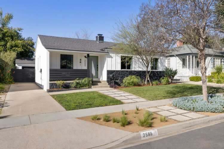 exterior of a traditional home with white board and batten, black stones, and a grey roof along with drought tolerant landscaping