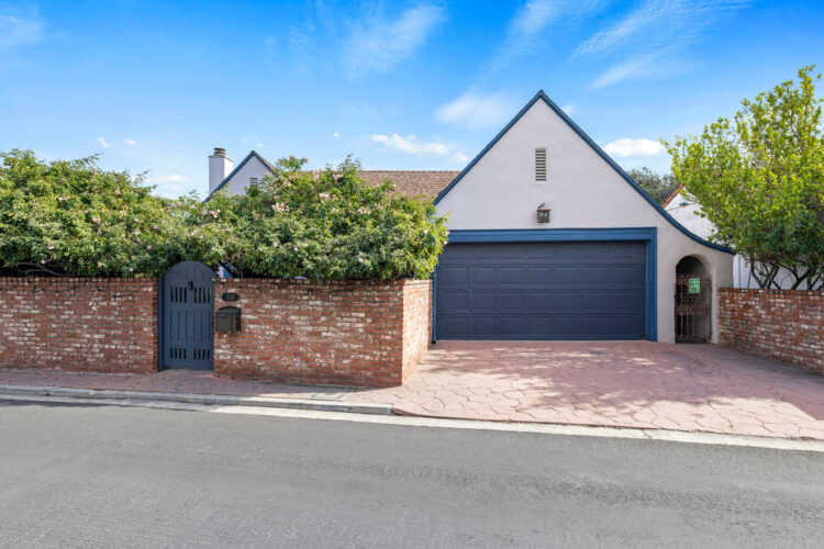 exterior of a tudor style home painted white with blue trim and garage door and brick wall with green hedges