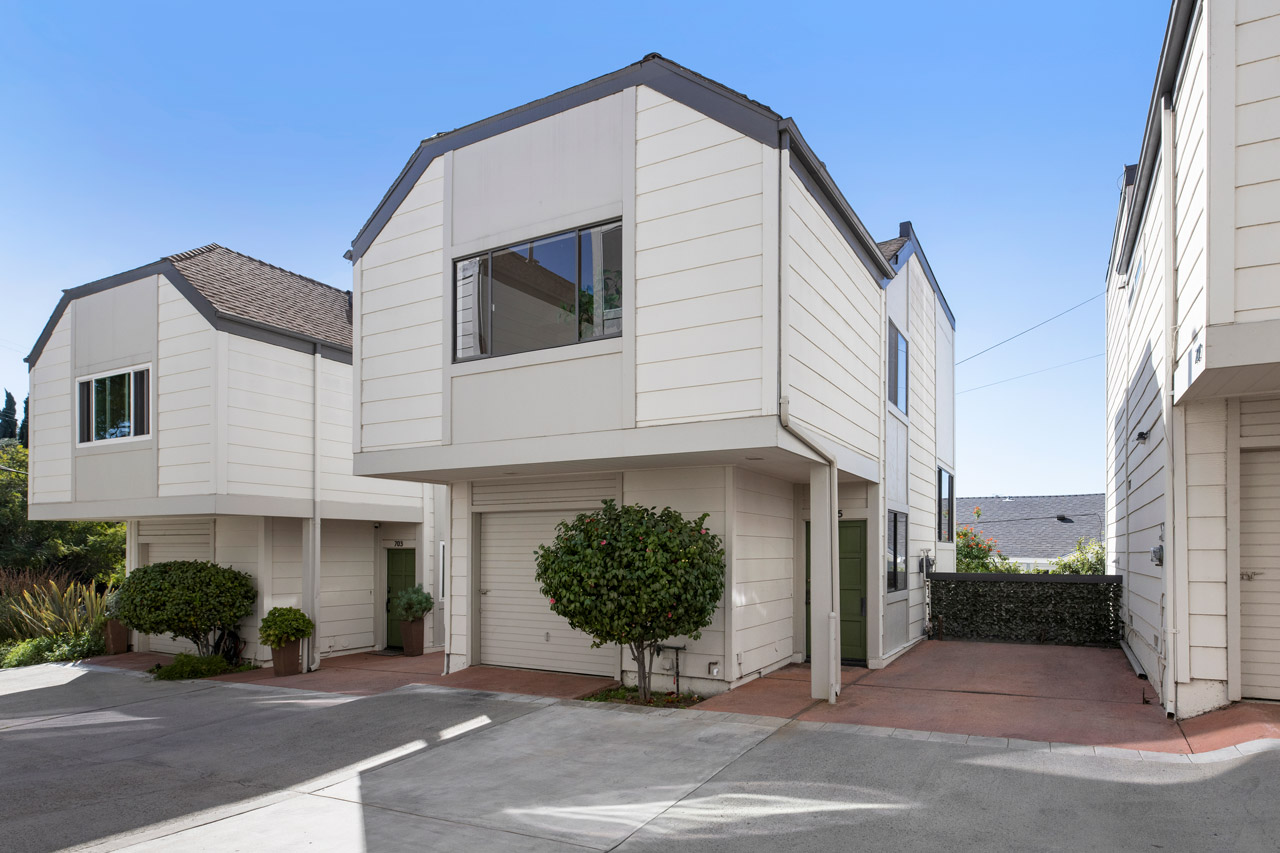 exterior of a three story condo painted white with green bush and one car garage