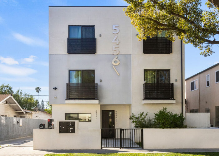 exterior of a three story contemporary apartment building painted white with black trim and a green tree