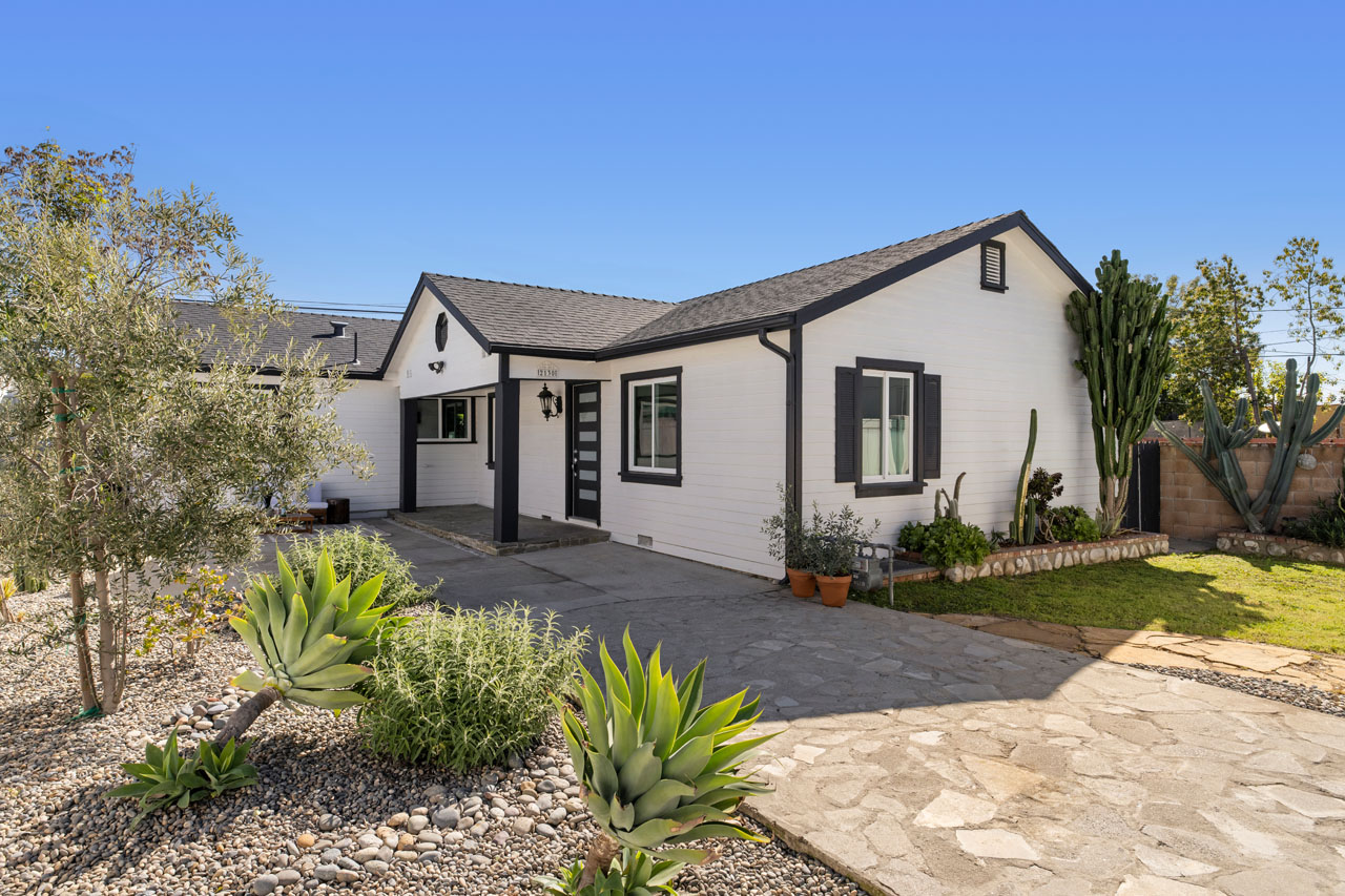 exterior of a rach style home painted white with black trim and stylish native landscaping