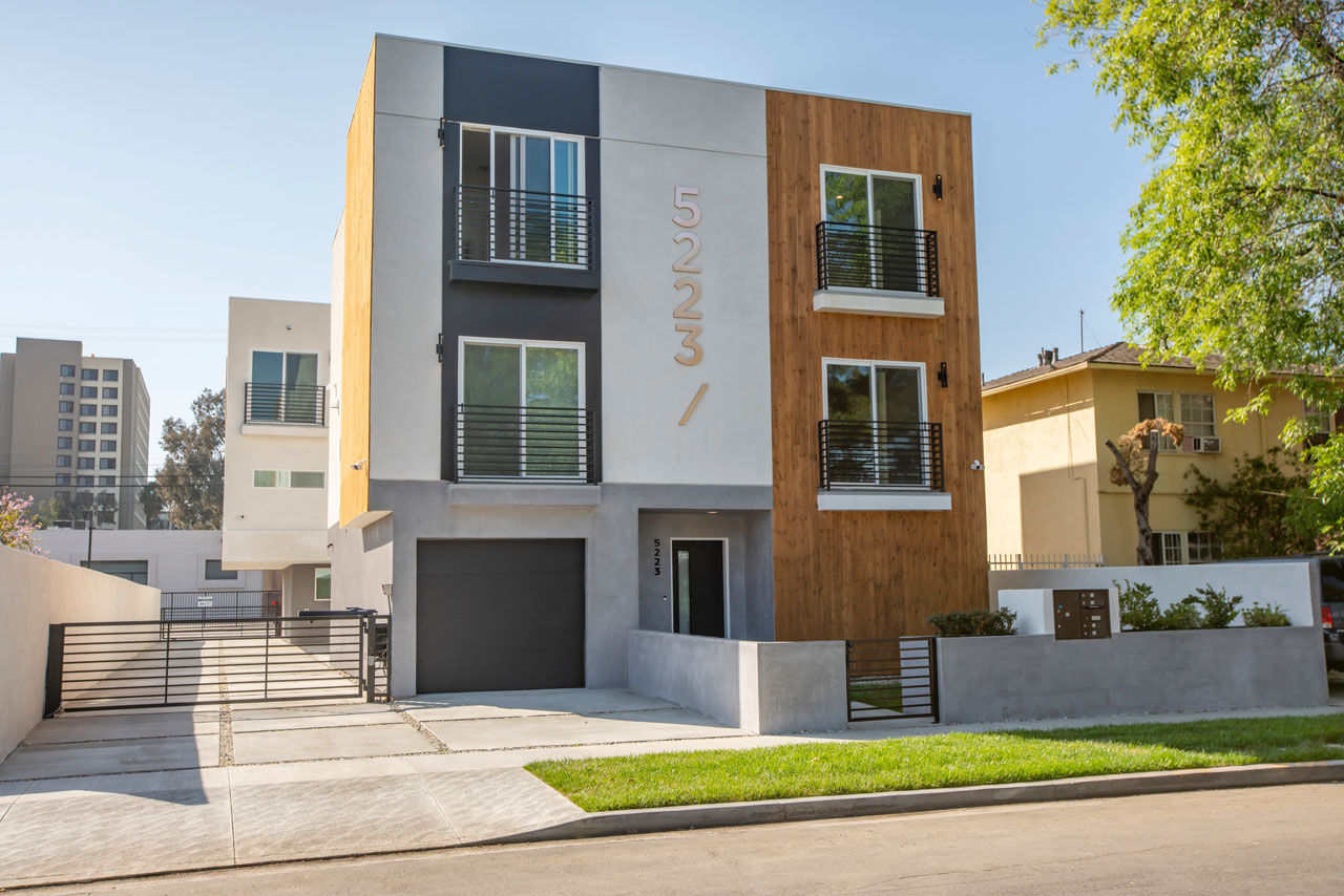 exterior of a contemporary three story townhouse building painted white, grey, with wood and a green yard