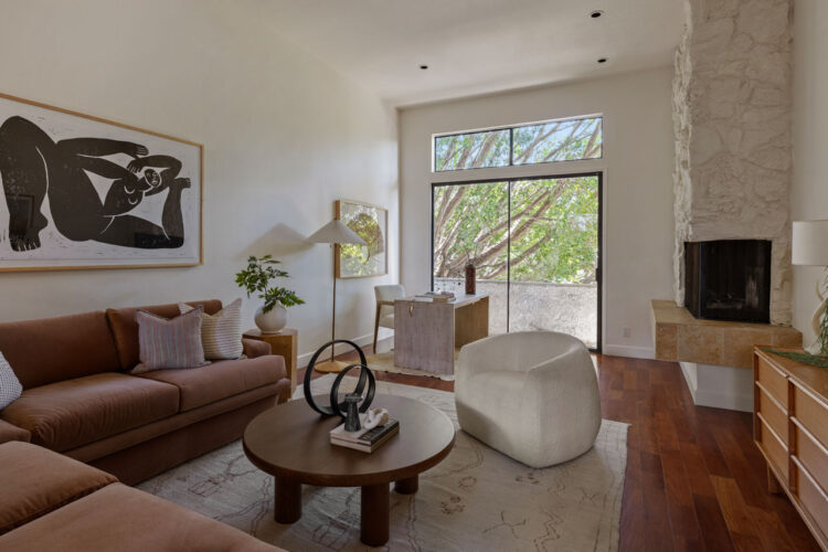 interior of a contemporary condo with couch, coffee table, and sliding glass doors opening to patio with green trees