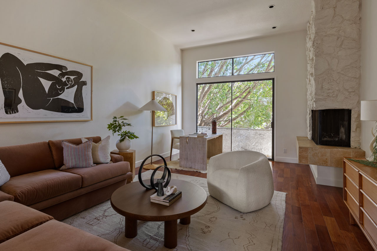 interior of a contemporary condo with couch, coffee table, and sliding glass doors opening to patio with green trees