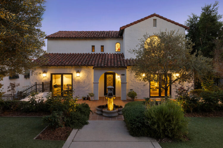 exterior of a spanish style estate home white stucco with saltillo tile roofs golden lights and green landscaping