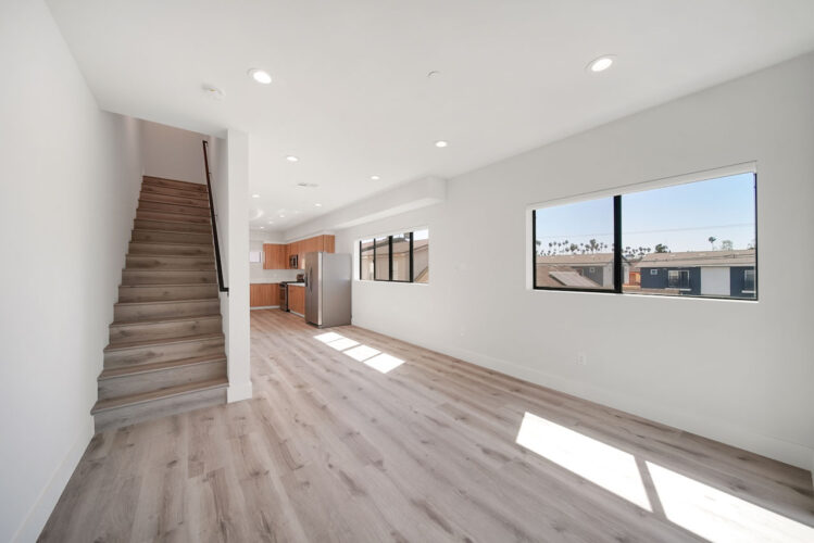 interior of a great room with stair case, kitchen with full appliance suite and windows looking out on sunny day