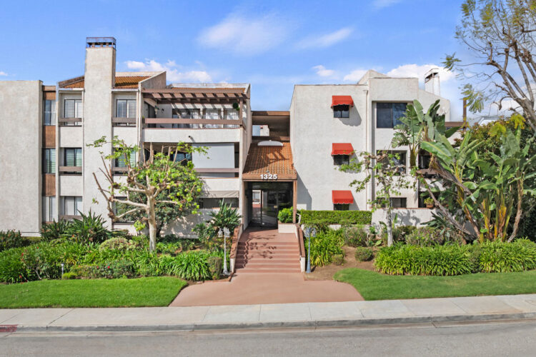 exterior of a three story condo building with light green stucco and red tile details